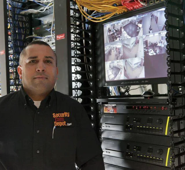 Luis from Security Cam Depot standing next to a commercial NVR and equipment rack